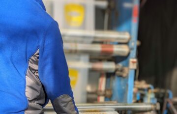 Працівник в навушниках біля станка, на якому виготовляють прозорі поліетиленові пакети з жовтим логотипом